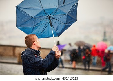 Rain in the city. Young man is holding blue umbrella during thunderstorm. Street of Prague, Czech Republic.  - Powered by Shutterstock