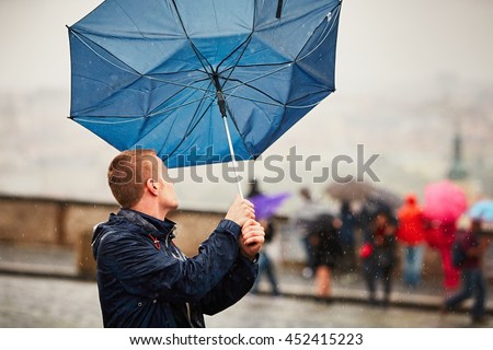 Rain in the city. Young man is holding blue umbrella during thunderstorm. Street of Prague, Czech Republic. 