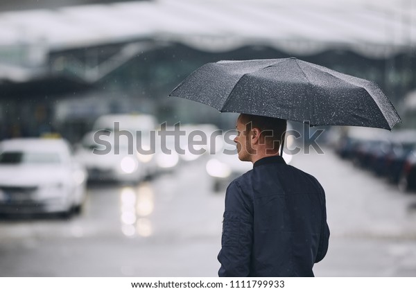 Rain in city. Young man holding umbrella walking in the\
street. 