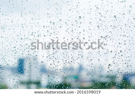 Rain drop on glass window at day time in monsoon season with blurred city buildings background.