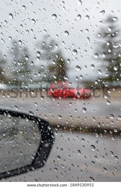 Rain droplets on a car side window, looking from the\
inside out to a defocused background of a suburban street on a\
cloudy  rainy day. A red car goes by. Selective focus background\
and copy space 