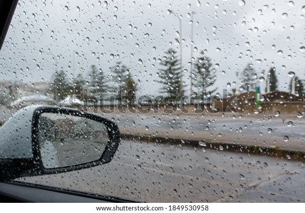 Rain droplets on a car side window, looking from\
the inside out to a defocused background of a suburban street on a\
cloudy  rainy day. Empty street in sight. Selective focus\
background and copy space