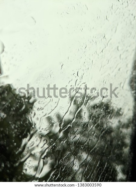 Rain droplets on car window with lush green\
colour background.