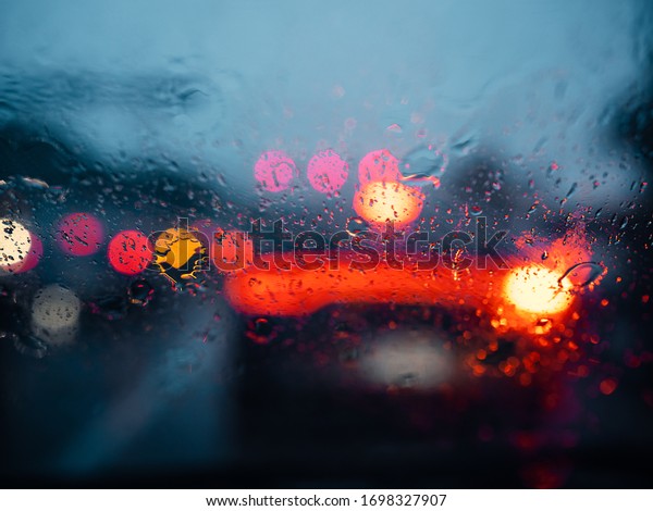 Rain droplets on car window with street bokeh in the\
background. 