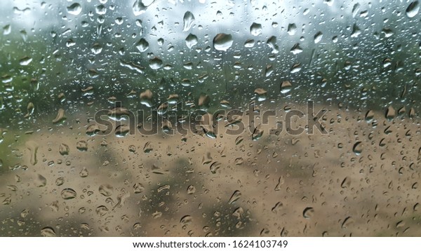 Rain droplets on the outside of a car window set\
against a sandy forest