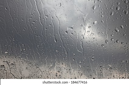 Rain Droplets On A Window Glass Pane With Dark Stormy Clouds In The Background. 