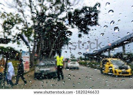 Rain droplets or raindrops on car window glass surface with roadside background