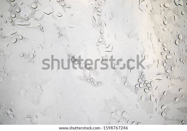 Rain\
droplets sit static on a glass window\
sunroof.