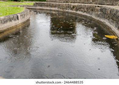 Rain drops causing circular ripples on a stone walled ornamental ponds surface