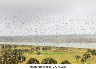 Rain Drops Covering A Window During A Storm With A View Of The Guadiana RIver In Southern Spain And A Golf Course Behind The Window.