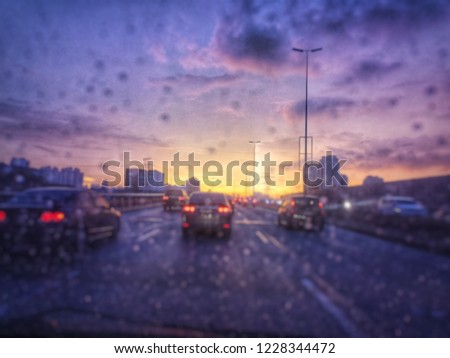 Rain drops dripping flow down the wind screen of the car with a blur focus of traffic, cars and lights with dusking sky in the background

