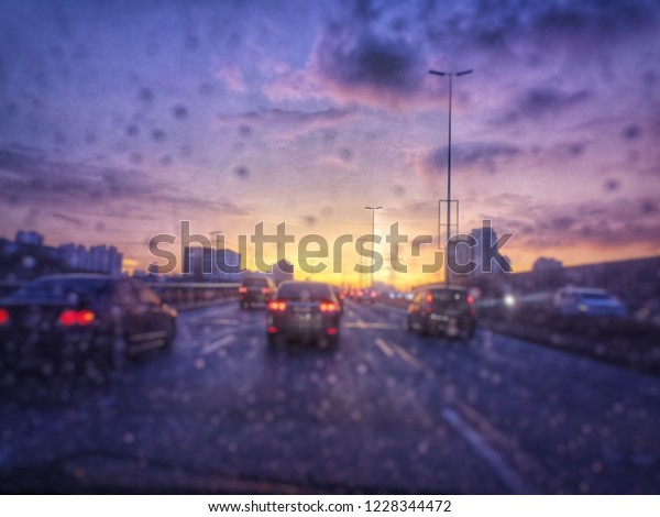 Rain drops dripping flow down the wind\
screen of the car with a blur focus of traffic, cars and lights\
with dusking sky in the\
background\
\
