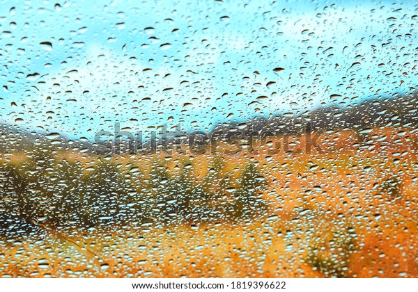 Rain\
drops falling on car window. Driving in rain. Nature landscape\
through glass. Autumn weather and road trip\
concept