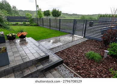 Rain drops falling on paved patio, green lawn, gravel, and bark mulch