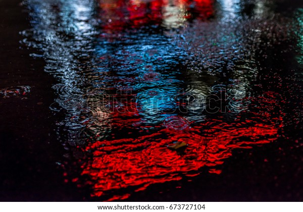 雨がアスファルトの上のプールに落ちる 夜の都市の背景に雨の中に水たまり 水の反射光 ナイトシティ 路上の水たまりに赤い光が映る運命の夜 の写真素材 今すぐ編集