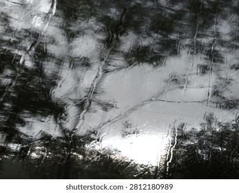 Rain Drops on Bus Window During Heavy Storm, Dark Gloomy Day 
Abstract view through a bus window during heavy rain. Raindrops and water streaks cover the glass, blurring the dark trees and gray sky outside. Moody, dramatic, and melancholic atmosphere with soft light breaking through the clouds. Perfect for background, weather, travel, emotion, loneliness, and rainy day concepts.
