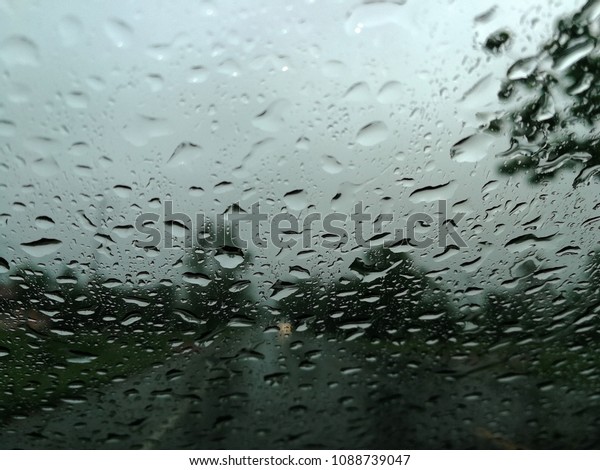 Rain drops on the car glass window\
with road in rainy season abstract background, water drop on the\
glass, night storm raining car driving\
concept.\