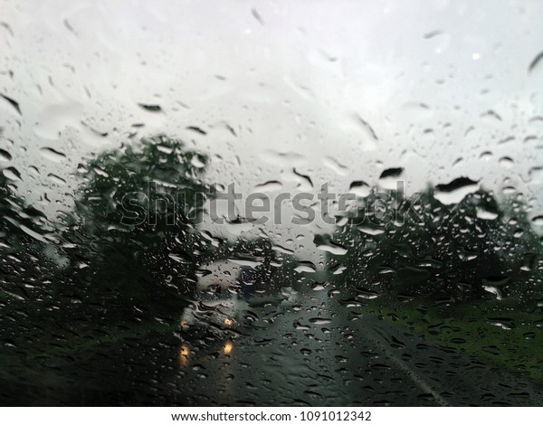 Rain drops on the car glass window\
with road in rainy season abstract background, water drop on the\
glass, night storm raining car driving\
concept.\
