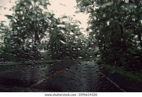 Rain drops on the car glass window\
with road in rainy season abstract background, water drop on the\
glass, night storm raining car driving\
concept.\
