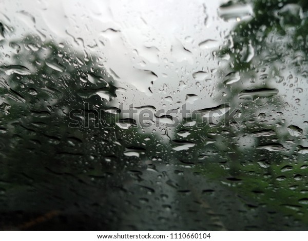 Rain drops on the car glass window\
with road in rainy season abstract background, water drop on the\
glass, night storm raining car driving\
concept.\
