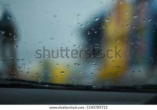 Rain drops on the car glass while the car is\
red. On the city street\
