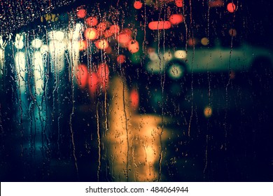 Rain Drops On Car Window With Road Light Bokeh, City Life In Night In Rainy Season Abstract Background,water Drop On The Glass, Night Storm Raining Car Driving Concept.