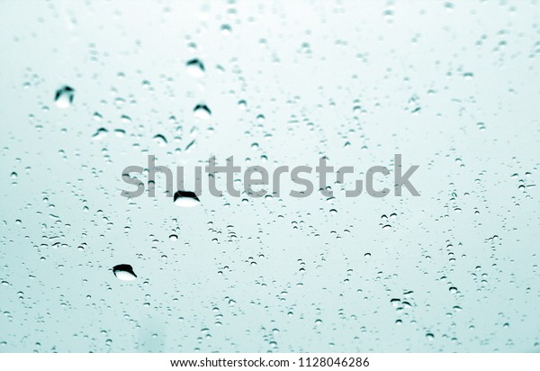 Rain drops on car window in cyan\
tone with blur effect. Abstract background and\
texture.