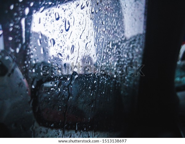 Rain\
drops on the car\'s window after a heavy rain in the evening. The\
side mirror shows blurry reflection of the car behind. At the\
background, the building can be seen in blur\
state.