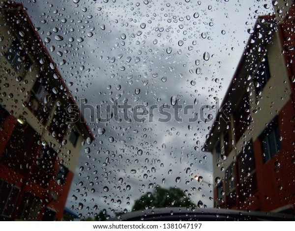 Rain drops on glass car window with road light\
bokeh. Stock image of rain drops on car glass in rainy season\
abstract background, water drop on the glass, night storm raining\
car driving concept