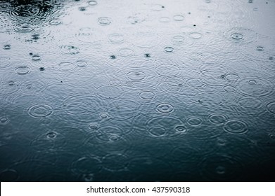 rain drops on the surface of water in a puddle with graduated shade of black shadow and reflection of blue sky 