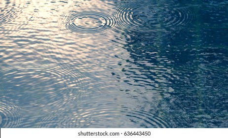 Rain Drops On The Swimming Pool Blue Water Surface That Have Ripple Wave Effect On Liquid Texture And Top View Angle.