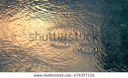 Rain drops on the water pool blue color surface that have ripple wave effect on liquid texture and top view angle. 
