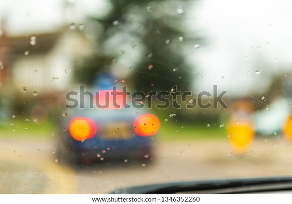 rain drops on the window of a car and smudged\
cars and people and pedestrians. raindrops in focus and blurred\
background.