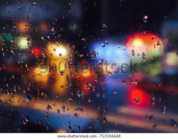 Rain drops on a window during the rain in a city.\
Background with blurred lights from cars on the road. Lights of\
different colors.
