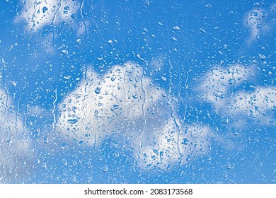 Rain drops on window glasses surface with blue sky and clouds background. Natural backdrop of raindrops. The concept of changing from rainy to sunny weather.