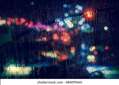 Rain Drops On Window With Road Light Bokeh, City Life In Night In Rainy Season Abstract Background,water Drop On The Glass, Night Storm Raining Car Driving Concept.