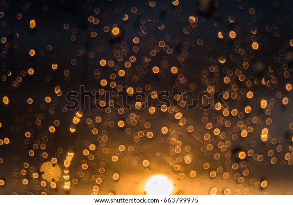 Rain drops on windows at night time with\
black bokeh background.
