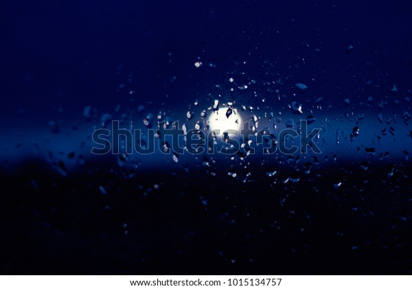 Rain drops texture on window glass with stunning\
blue violet moon light abstract blurred cityscape skyline bokeh\
background. Soft focus