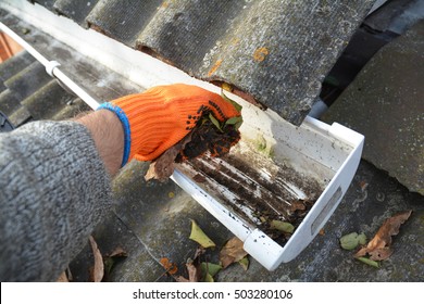 Rain Gutter Cleaning From Leaves In Autumn With Hand.  Roof Gutter Cleaning Tips. Clean Your Gutters Before They Clean Out Your Wallet. Step By Step. Gutter Cleaning.