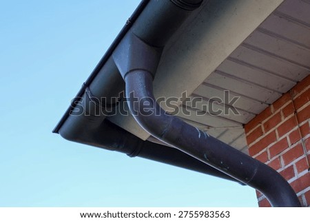 Rain gutter and downspout system capturing rainwater from a building roof against a blue sky