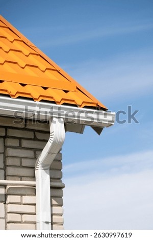 Rain Gutter Pipeline System on brick house , bright orange metal tile roof against blue sky