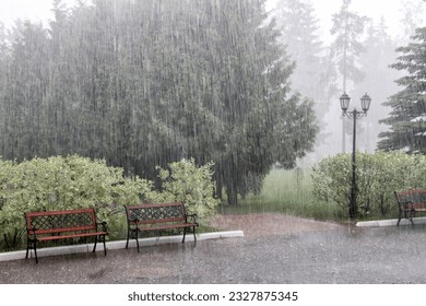 Rain with hail on a summer day. Large puddles on the sidewalk during heavy rain. Heavy rain in the park. Wet benches on a paved path. Spray drops and bubbles in large puddles. - Shutterstock ID 2327875345