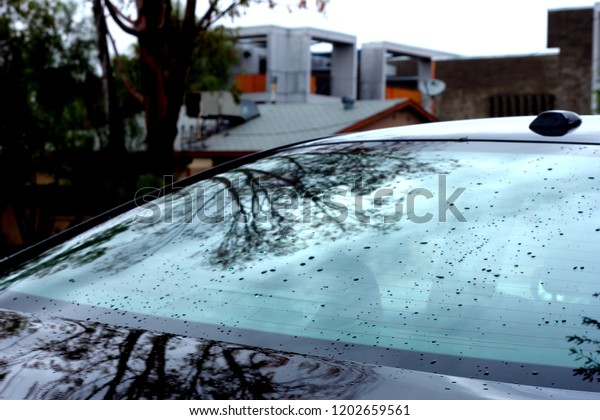 Rain on\
a car rear windshield in an urban\
environment