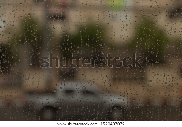 Rain\
on a window looking out there are cars on the\
road.