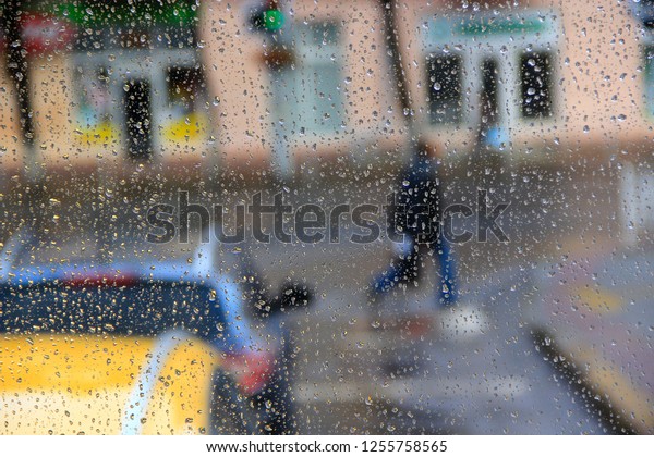 Rain outside window on background of city life.\
Drops of water dropping on glass during rain. Passers-by pass\
street in rain. Droplets of water beyond window glass during\
raining. Rain in city