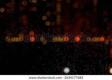 Rain patters against a window, distorting the vibrant city lights into a bokeh blur. The droplets cling to the glass, creating an abstract, impressionistic view of the cityscape.