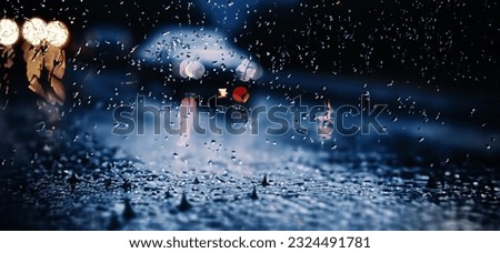 Rain shower on car windshield or car window and blurry road in background. Driving in rainy season. Rain drops on car mirror. Traffic road in evening rain. Drizzle raining decreases driving visibility