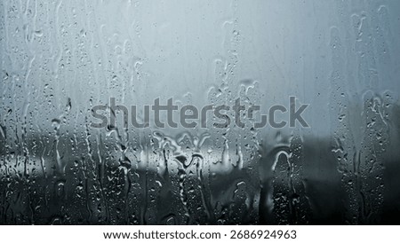 Rain streaking down a window pane with a blurred, gloomy cityscape in the background.