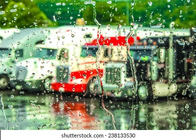 Rain streaming down a window with 18 wheeler trucks in the background.