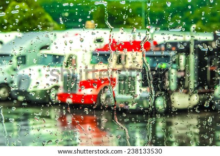 Rain streaming down a window with 18 wheeler trucks in the background.